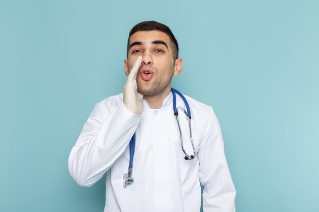 Vista frontal del joven médico en traje blanco con estetoscopio azul susurrando