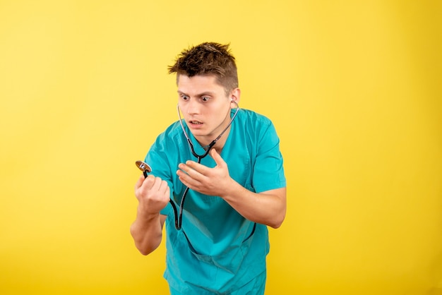 Vista frontal joven médico en traje médico con estetoscopio en escritorio amarillo