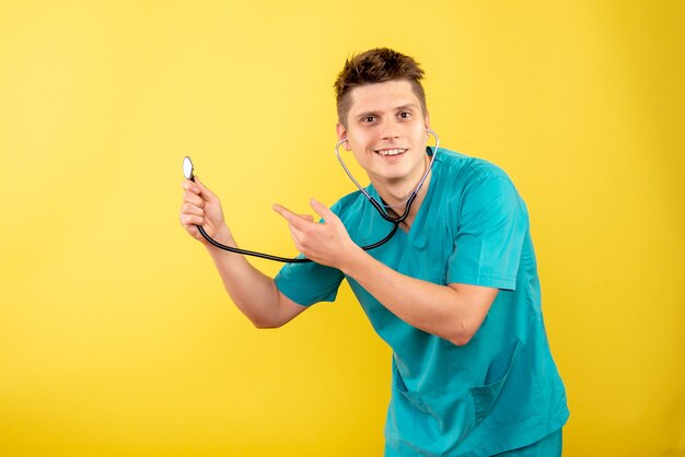 Vista frontal joven médico en traje médico con estetoscopio sobre fondo amarillo