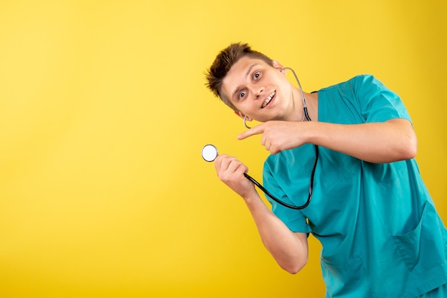 Vista frontal joven médico en traje médico con estetoscopio sobre fondo amarillo