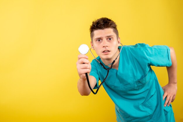 Vista frontal joven médico en traje médico con estetoscopio sobre fondo amarillo