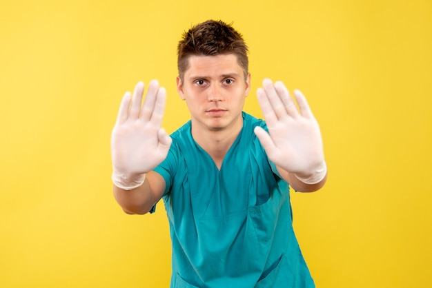 Vista frontal joven médico en traje médico con guantes sobre fondo amarillo