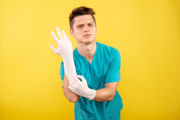 Vista frontal joven médico en traje médico con guantes sobre fondo amarillo