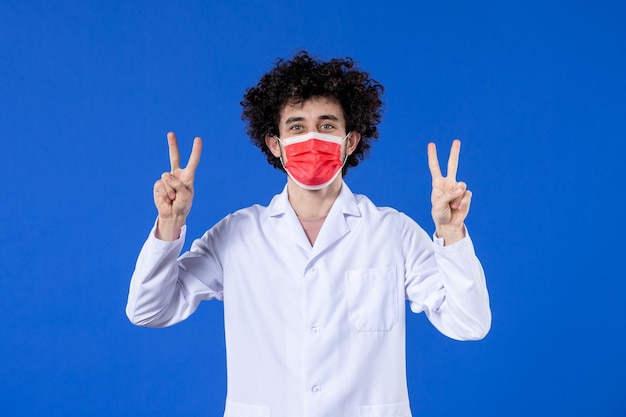 Vista frontal joven médico en traje médico con máscara roja sobre fondo azul virus droga covid- medicina pandémica vacuna salud