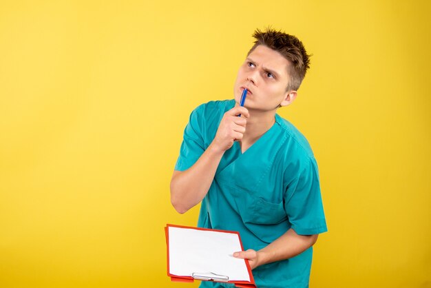 Vista frontal joven médico en traje médico con notas sobre fondo amarillo