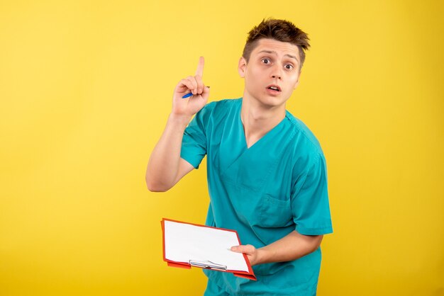 Vista frontal joven médico en traje médico con notas sobre fondo amarillo