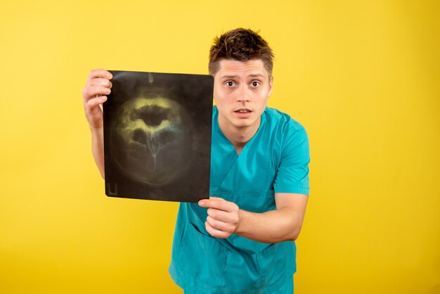 Vista frontal joven médico en traje médico con rayos x sobre fondo amarillo