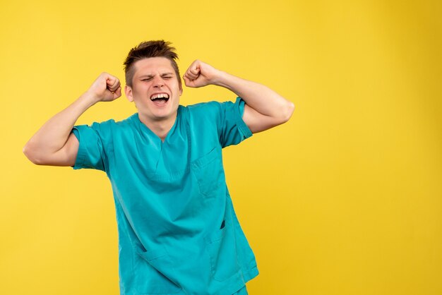 Vista frontal joven médico en traje médico regocijándose emocionalmente sobre fondo amarillo