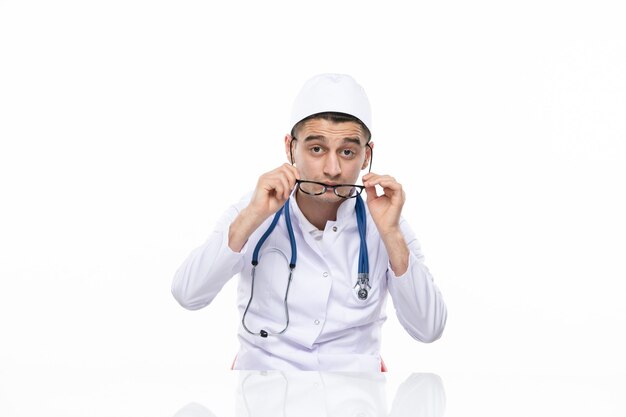 Vista frontal joven médico en traje médico sentado detrás del escritorio