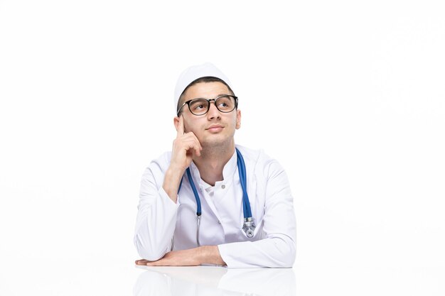 Vista frontal joven médico en traje médico sentado detrás del escritorio