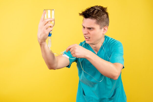 Vista frontal joven médico en traje médico sosteniendo gotero sobre fondo amarillo