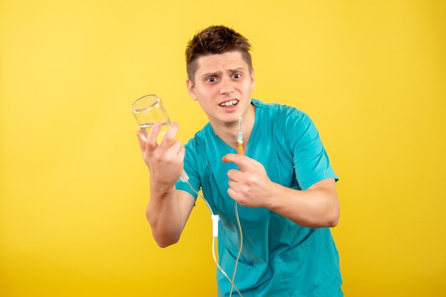 Vista frontal joven médico en traje médico sosteniendo gotero sobre fondo amarillo