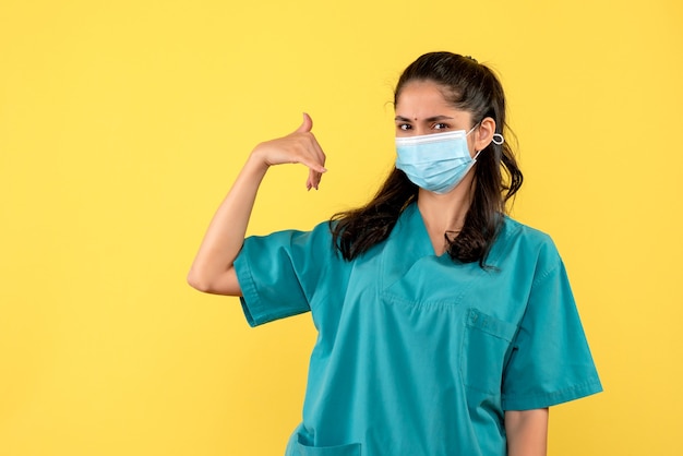 Foto gratuita vista frontal joven médico en uniforme haciendo llamarme señal de teléfono de pie sobre fondo amarillo