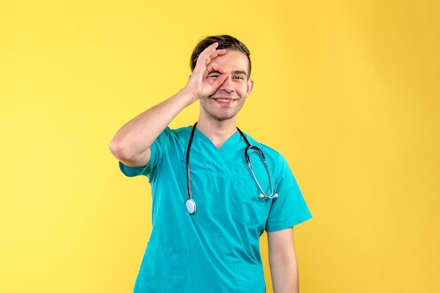 Vista frontal del joven médico varón sonriendo sobre pared amarilla