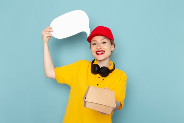 Vista frontal joven mensajero en camisa amarilla y capa roja con paquete de alimentos y letrero blanco en el espacio azul