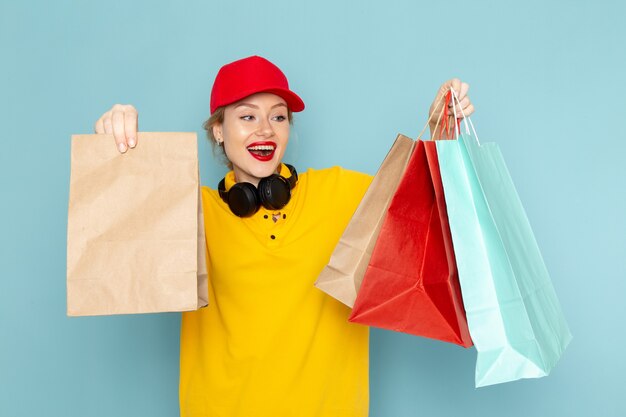 Vista frontal joven mensajero con camisa amarilla y capa roja sosteniendo paquetes de compras y multiplicar en el espacio azul