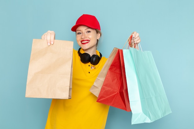 Vista frontal joven mensajero con camisa amarilla y capa roja sosteniendo paquetes de compras y multiplicar en el espacio azul