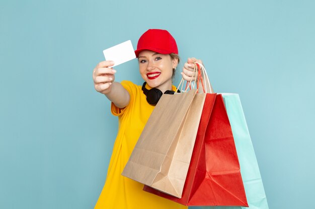 Vista frontal joven mensajero con camisa amarilla y capa roja sosteniendo paquetes de compras y multiplicar en el trabajador espacial azul