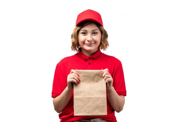Una vista frontal joven mensajero en camisa roja gorra roja sosteniendo el paquete de entrega sonriendo