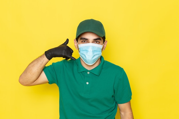 Vista frontal joven mensajero en camisa verde gorra verde guantes negros mostrando señal de llamada telefónica en amarillo