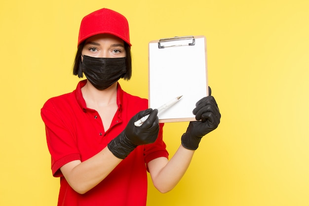 Una vista frontal joven mensajero femenino en rojo uniforme guantes negros y gorra roja con bloc de notas