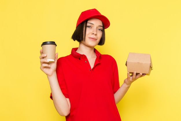 Una vista frontal joven mensajero femenino en rojo uniforme guantes negros y gorra roja con caja de comida y taza de café