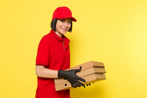 Una vista frontal joven mensajero femenino en rojo uniforme guantes negros y gorra roja con cajas de comida