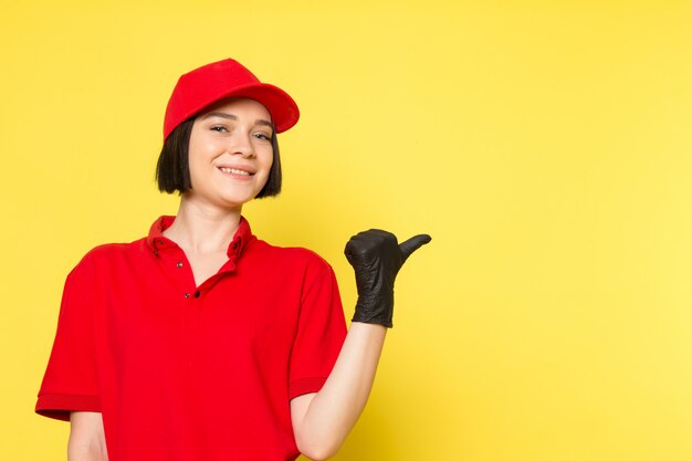 Una vista frontal joven mensajero femenino en rojo uniforme guantes negros y gorra roja posando