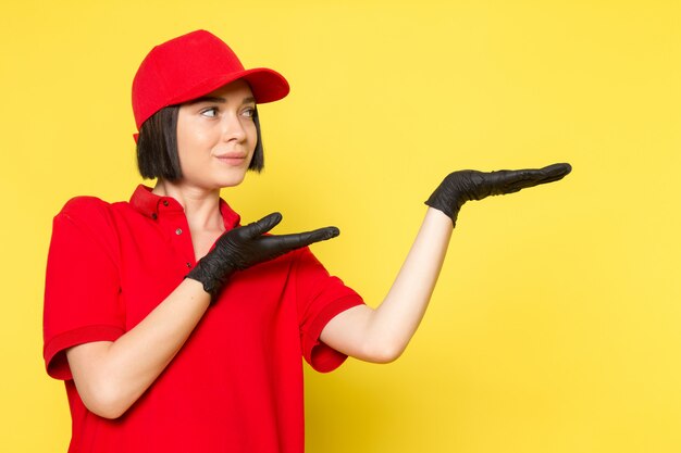 Una vista frontal joven mensajero femenino en rojo uniforme guantes negros y gorra roja posando