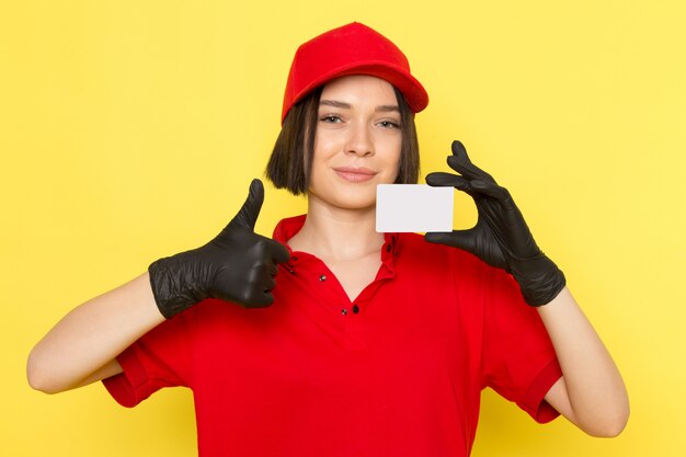 Una vista frontal joven mensajero femenino en rojo uniforme guantes negros y gorra roja con tarjeta blanca