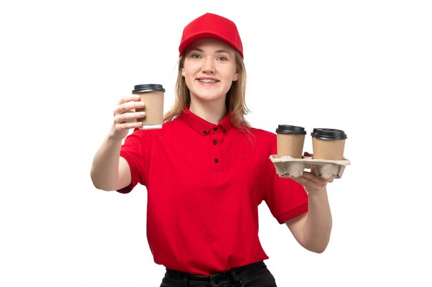 Una vista frontal joven mensajero femenino trabajadora del servicio de entrega de alimentos sonriendo sosteniendo café en blanco