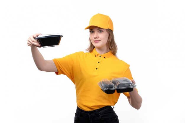 Una vista frontal joven mensajero femenino trabajadora del servicio de entrega de alimentos sonriendo sosteniendo cuencos con comida en blanco