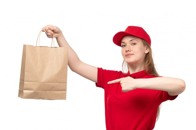 Una vista frontal joven mensajero femenino trabajadora del servicio de entrega de alimentos sonriendo sosteniendo el paquete de entrega de alimentos en blanco