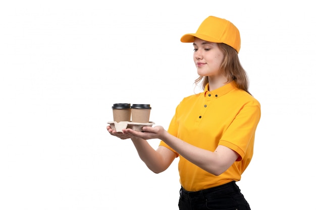 Una vista frontal joven mensajero femenino trabajadora del servicio de entrega de alimentos con tazas de café sonriendo en blanco