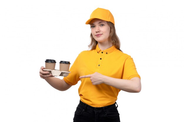 Una vista frontal joven mensajero femenino trabajadora del servicio de entrega de alimentos con tazas de café sonriendo en blanco