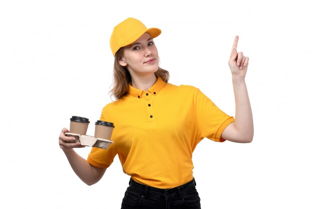 Una vista frontal joven mensajero femenino trabajadora del servicio de entrega de alimentos con tazas de café sonriendo en blanco