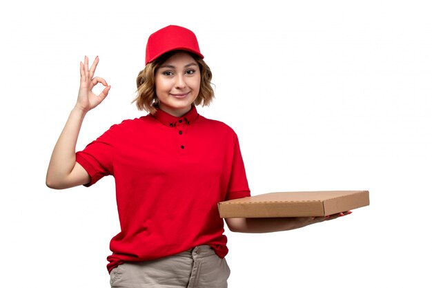 Una vista frontal joven mensajero trabajadora del servicio de entrega de alimentos con paquete de entrega de alimentos sonriendo en blanco