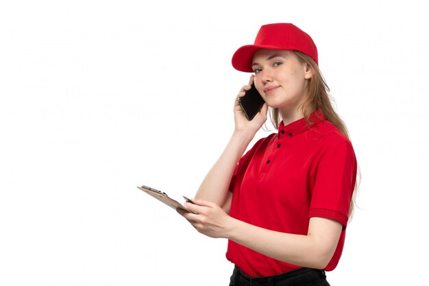 Una vista frontal joven mensajero trabajadora del servicio de entrega de alimentos sonriendo hablando por teléfono con bloc de notas en blanco