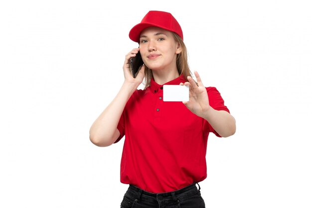 Una vista frontal joven mensajero trabajadora del servicio de entrega de alimentos sonriendo hablando por teléfono y sosteniendo la tarjeta blanca sobre blanco