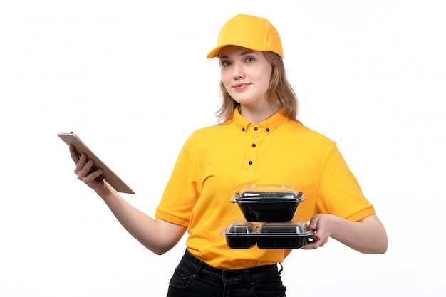 Una vista frontal joven mensajero trabajadora del servicio de entrega de alimentos sonriendo sosteniendo el bloc de notas para firmas y cuencos con comida en blanco