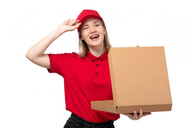 Una vista frontal joven mensajero trabajadora del servicio de entrega de alimentos sonriendo sosteniendo la caja con comida en blanco