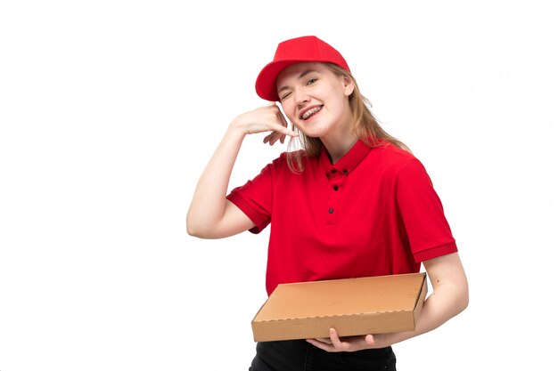 Una vista frontal joven mensajero trabajadora del servicio de entrega de alimentos sonriendo sosteniendo la caja con comida posando en blanco