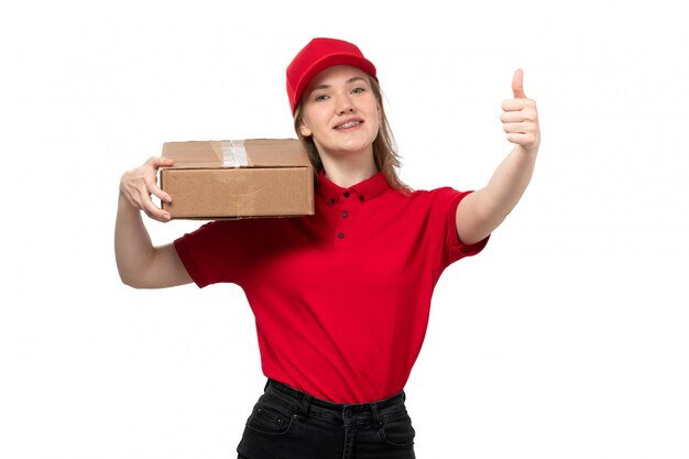 Una vista frontal joven mensajero trabajadora del servicio de entrega de alimentos sonriendo sosteniendo la caja de entrega en blanco