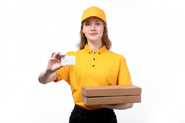 Una vista frontal joven mensajero trabajadora del servicio de entrega de alimentos sonriendo sosteniendo cajas de entrega de alimentos y una tarjeta blanca sobre blanco