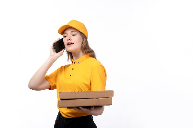 Una vista frontal joven mensajero trabajadora del servicio de entrega de alimentos sonriendo sosteniendo cajas de entrega y hablando por teléfono en blanco