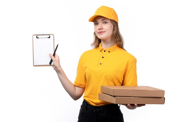 Una vista frontal joven mensajero trabajadora del servicio de entrega de alimentos sonriendo sosteniendo cajas de pizza y un bloc de notas en blanco