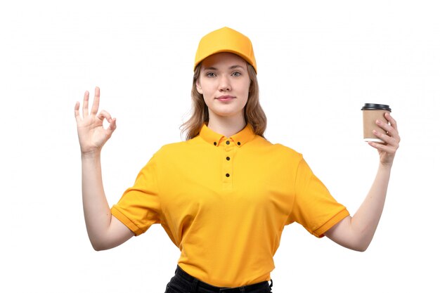 Una vista frontal joven mensajero trabajadora del servicio de entrega de alimentos sosteniendo una taza de café sonriendo en blanco