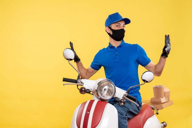 Vista frontal joven mensajero en uniforme azul sobre fondo amarillo covid- trabajo servicio de entrega de pandemias virus trabajo en bicicleta