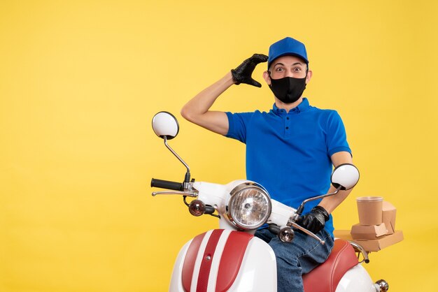 Vista frontal joven mensajero en uniforme azul sobre fondo amarillo trabajo covid- servicio de entrega de trabajo virus bike