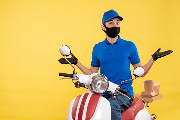 Vista frontal joven mensajero en uniforme azul sobre fondo amarillo trabajo de virus de servicio de entrega de pandemia de trabajo covid